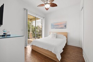 Un dormitorio con cama, ventilador de techo, ventana con vistas y un cuadro en la pared.