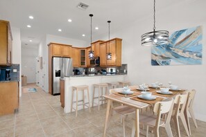 Uma cozinha moderna com armários de madeira, eletrodomésticos de aço inoxidável e uma área de jantar com uma mesa posta para quatro pessoas.