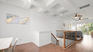 A spacious room with hardwood flooring, a white ceiling with recessed lighting, a staircase with a wooden railing, and a large window offering a view of the outdoors. - Game Room Arcade Games Private Pool Guest House-7521 (Kissimmee)