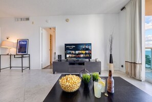 A modern living room with a flat-screen TV displaying Prime Video, a bowl of popcorn, a bottle of drink, and a small potted plant on a dark coffee table. - Hollywood Oasis Familiar |Playa | Piscina | Balcón (Hollywood)