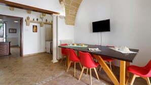 A dining area with a long table, red chairs, a television mounted on the wall, and a stone ceiling. - Holiday Home "Dimora Collina 1" with Wi-Fi and Air Conditioning (Sannicola)