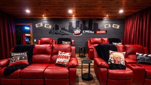Una habitación temática de cine con sofás de cuero rojo, almohadones con motivos de palomitas de maíz y una pared decorada con elementos relacionados al cine.