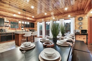 Ein Holzinterieur mit Essbereich für sechs Personen, Küchenschränken und einem großen Fenster mit Vorhängen.