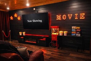 A cozy movie theater with a large screen displaying 'Now Showing,' popcorn machines, and a red velvet rope barrier. - Brand New Design! Huge Pool Cabin@ Blackhawk Lodge (Sevierville)