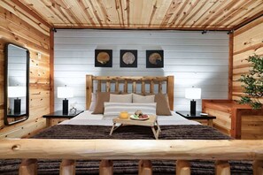 Ein Schlafzimmer einer Holzhütte mit einem Bett, Nachttischlampen, einem Tablett mit Speisen und drei an der Wand befestigten Bildern.