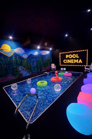 A pool with colorful floating rings, a neon sign reading 'POOL CINEMA', and a mural of a sunset. - Brand New Design! Huge Pool Cabin@ Blackhawk Lodge (Sevierville)