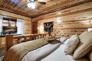 A wooden cabin room with a bed, a small table with a drink, and a TV on a wooden stand. - Brand New Design! Huge Pool Cabin@ Blackhawk Lodge (Sevierville)