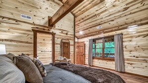 A log cabin bedroom with a large bed, a wooden ceiling, and a window with curtains. - Brand New Design! Huge Pool Cabin @ BIG STAR LODGE (Sevierville)