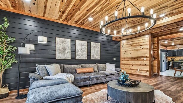 A modern living room with a dark wooden wall, a grey sofa, a round coffee table, and a hanging light fixture. - Brand New Design! Huge Pool Cabin @ BIG STAR LODGE (Sevierville)