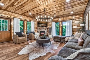 Ein gemütliches Wohnzimmer mit Kamin, Holzbalkendecke und großen Fenstern.