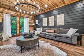 Un salon moderne avec un plafond en bois, une table basse ronde, un canapé gris et des œuvres d’art encadrées accrochées au mur.