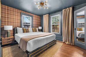 Une chambre moderne avec un grand lit, deux tables de chevet avec des lampes, un luminaire au plafond et une vue sur l’extérieur par les fenêtres.