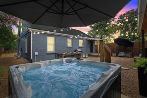 Un jardin avec un jacuzzi, une terrasse en bois, un patio couvert et une maison à l’extérieur en briques.