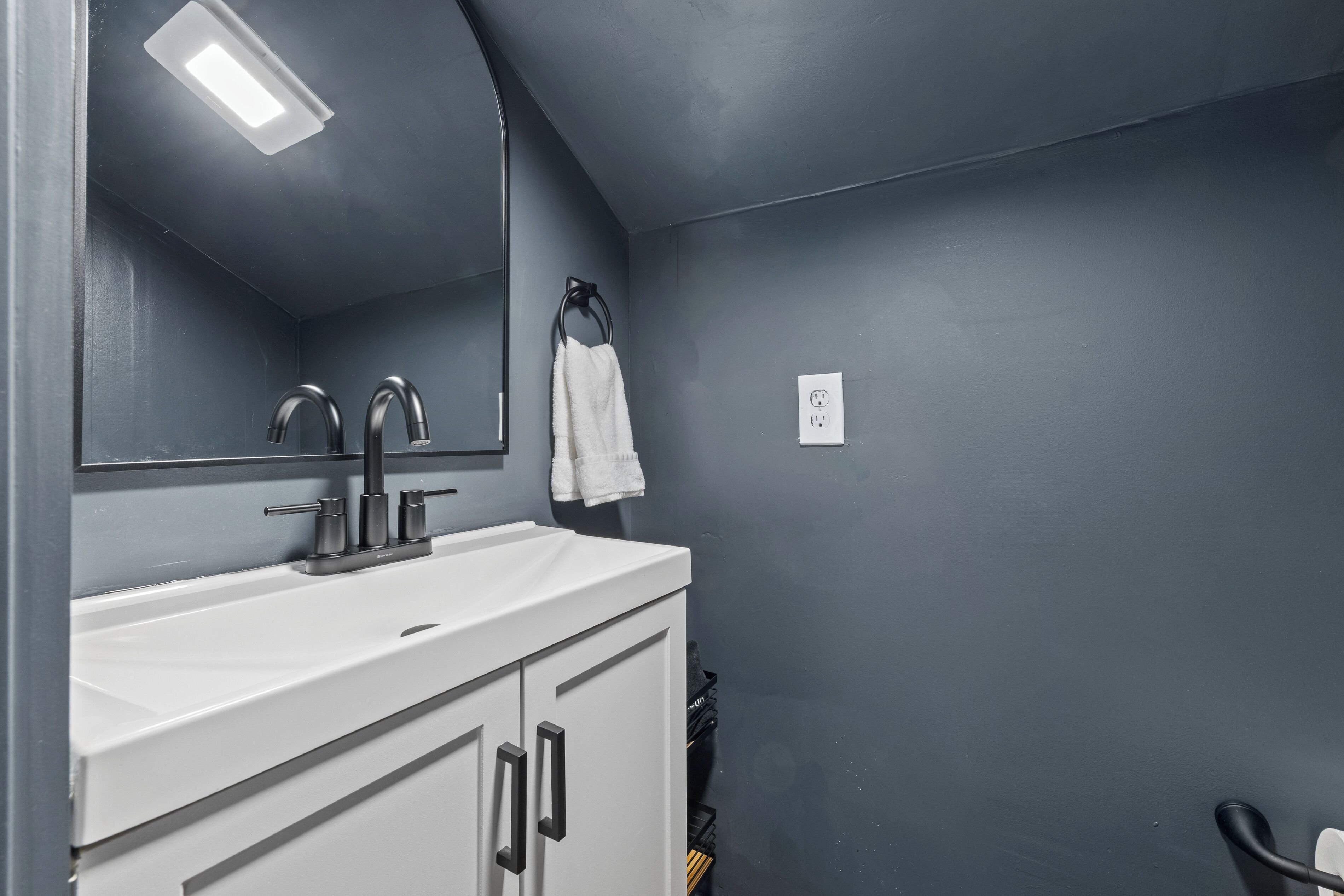 A bathroom with a white sink, two faucets, a mirror, a towel rack, and a light fixture.