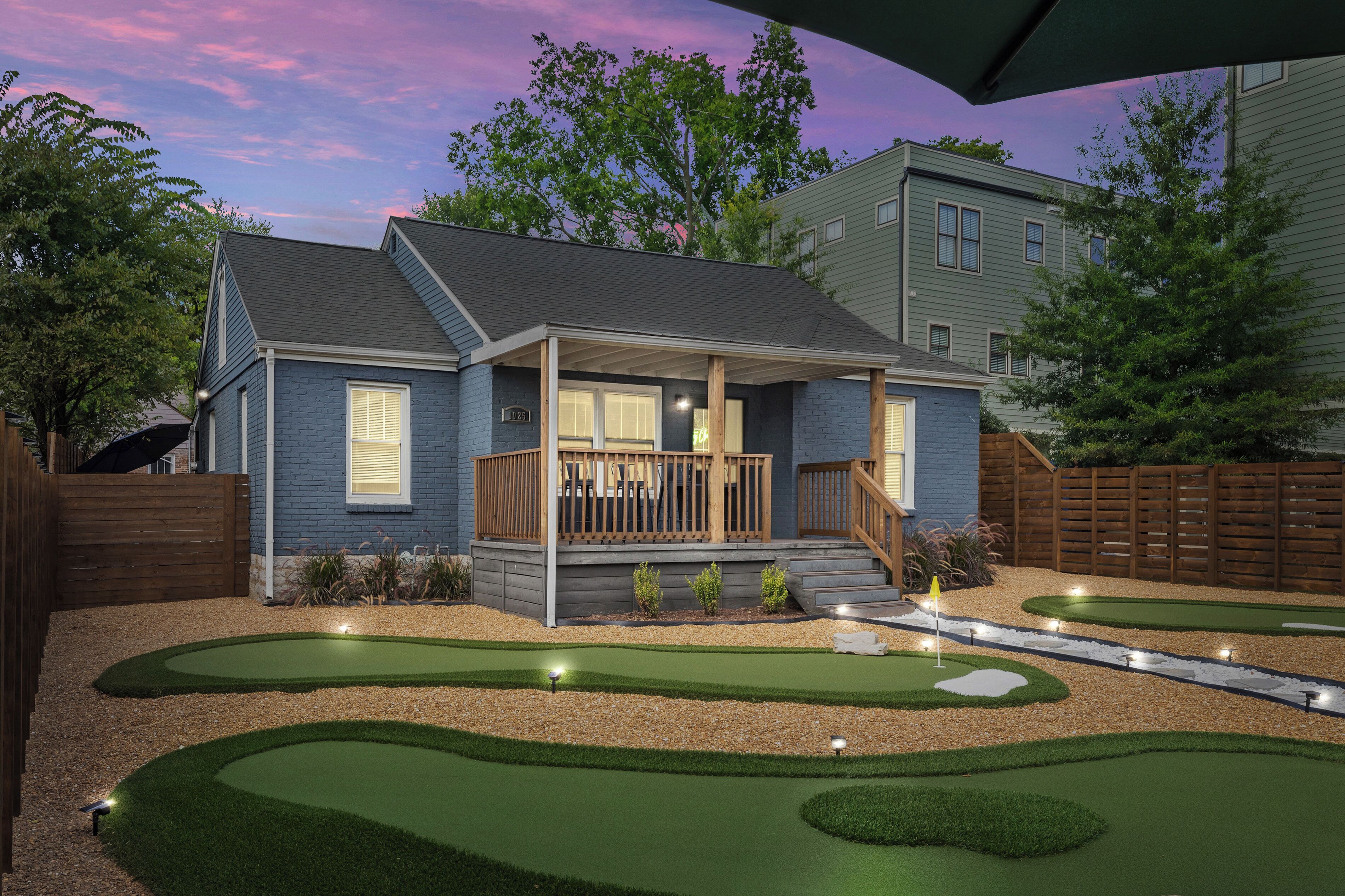 A residential property with a covered porch, a landscaped garden with a putting green, and a wooden fence.