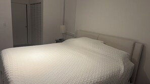 Ein Schlafzimmer mit einem Bett, einem Nachttisch, einer Lampe und einer Tür.