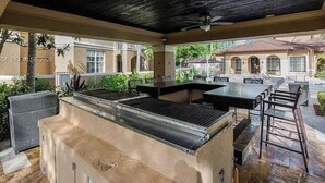 Un'area patio esterna con una postazione barbecue, posti a sedere e vista su un edificio con archi.