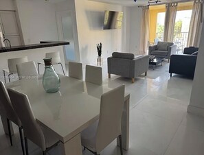 Una sala de estar moderna con comedor, un televisor de pantalla plana montado en la pared y un balcón con cortinas.