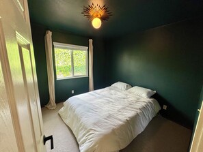 Un dormitorio con cama, ventana con cortinas y lámpara en el techo.