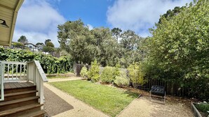A residential backyard with a lawn, a wooden deck, and a gravel pathway leading to a house entrance. - Monterey Getaway - Fabulous 3-bedroom house in Monterey (Monterey)