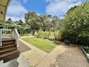 A residential backyard with a lawn, a wooden deck, and a gravel pathway leading to a house entrance. - Monterey Getaway - Fabulous 3-bedroom house in Monterey (Monterey)