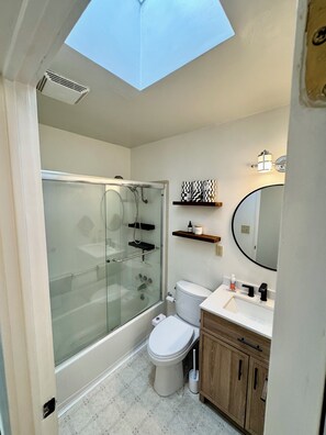 Un baño pequeño con ducha de vidrio, inodoro, lavabo con espejo y tragaluz.