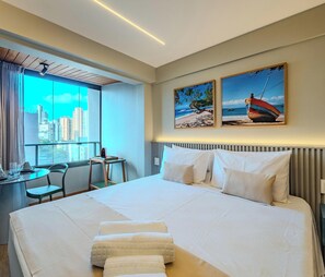 A hotel room with a large bed, a desk with a chair, and two framed pictures on the wall. - Barra with the beach and shopping nearby (Salvador)