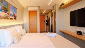 Hotellihuone, jossa on sänky, televisio, pieni keittopiste ja ovi, joka johtaa toiseen huoneeseen.