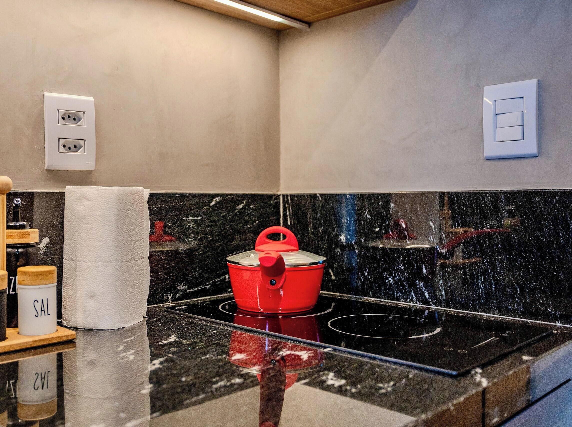 Une cuisine avec un plan de travail noir, une casserole rouge sur la cuisinière et un torchon blanc posé sur le plan de travail.