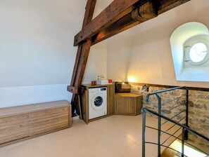 A laundry room with a washing machine, wooden bench, stone wall, and a window with a view. - Villa Teranga - Terre d'Accueil - Château Colin (Belleau)