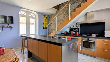 Una cocina moderna con una isla central, una escalera de piedra y un comedor con una mesa de mimbre.