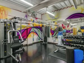 Ein Fitnessraum mit unterschiedlichen Trainingsgeräten, darunter eine Gewichtbank, Kurzhanteln und eine Klimmzugstange.