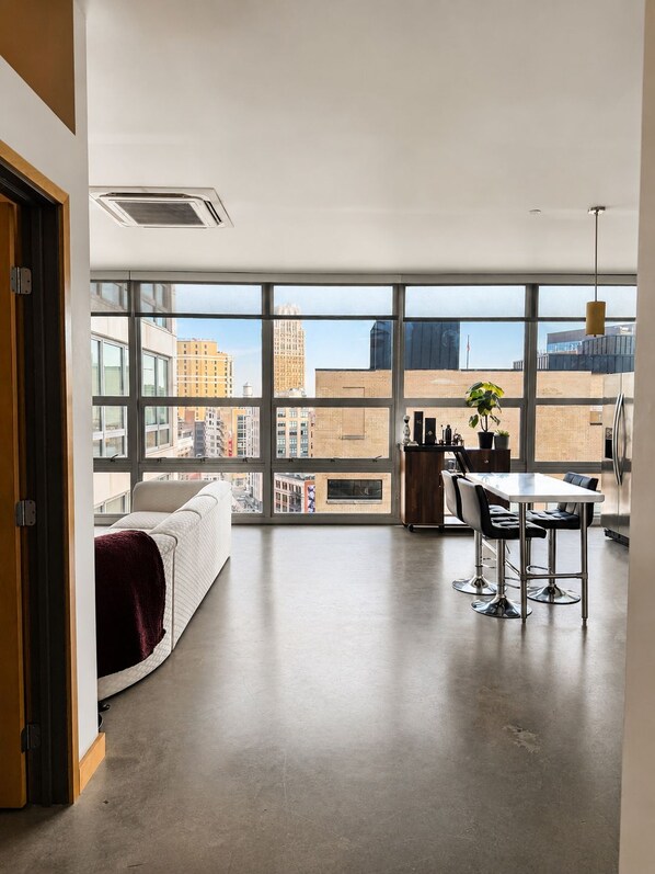 A modern apartment with a large window, a dining area, and a kitchen.