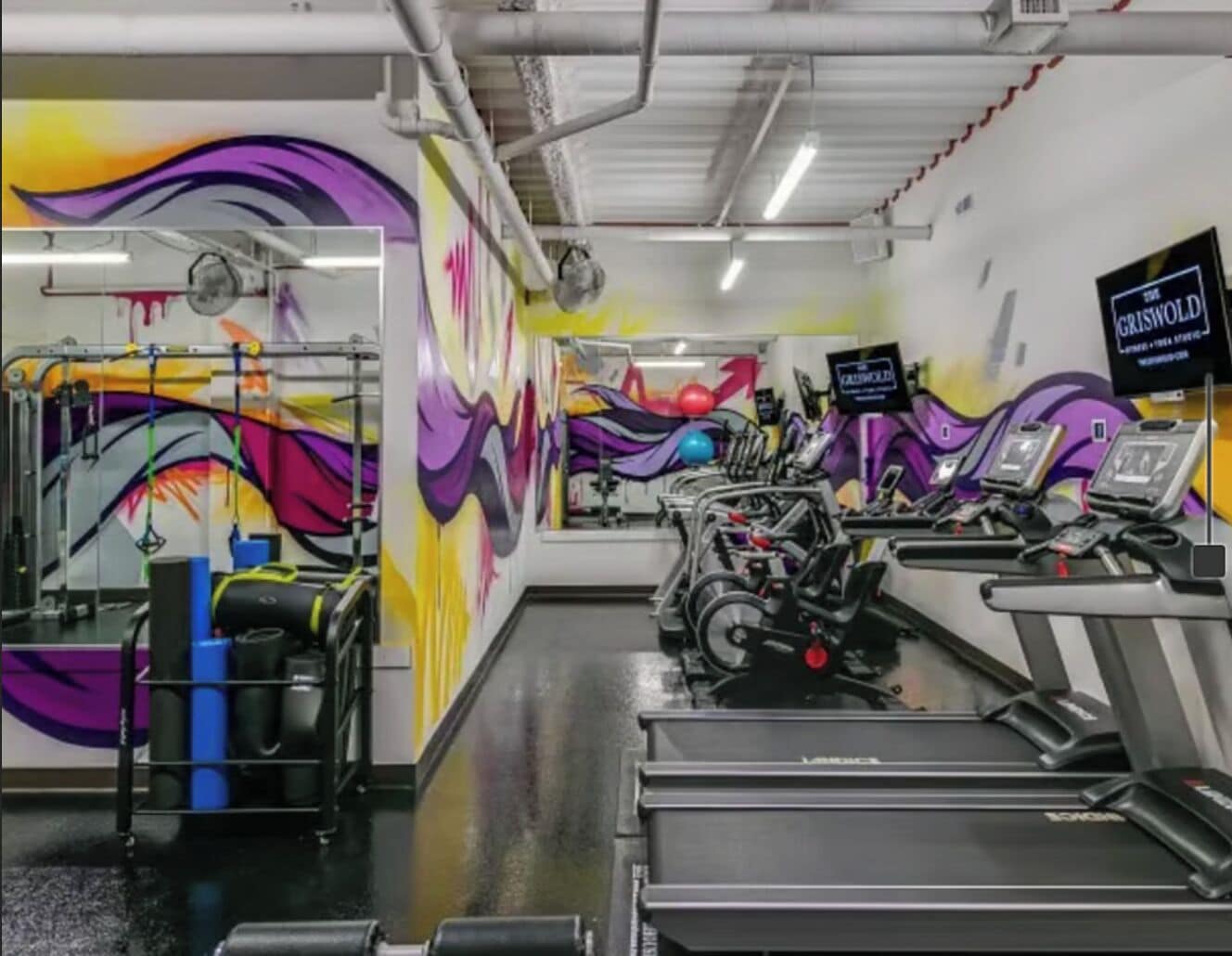 A gym with exercise equipment and a colorful mural on the wall.