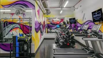 A gym with exercise equipment and a colorful mural on the wall.