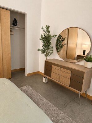 Ein Schlafzimmer mit einem Holzschrank, einem runden Spiegel, einer Zimmerpflanze und einem Nachttisch.