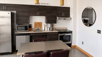 A modern kitchen with dark wood cabinets, stainless steel appliances, a round mirror, and a dining area with a wooden table and leather chairs.