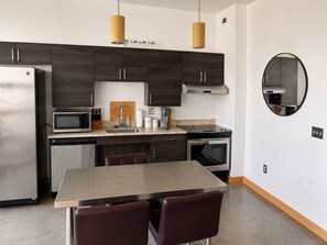 A modern kitchen with dark wood cabinets, stainless steel appliances, a round mirror, and a dining area with a wooden table and leather chairs.