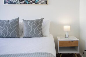 A neatly made bed with two pillows, a bedside table with a lamp, and a wall-mounted artwork. - Sandy Shores A Spacious Newcastle Beach Escape (Newcastle)