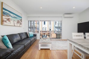 A modern living room with a leather sofa, a coffee table, and a dining area with chairs. - Sandy Shores A Spacious Newcastle Beach Escape (Newcastle)