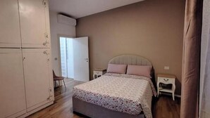 Un dormitorio con cama, mesitas de noche, un armario y una puerta que da a otra habitación.
