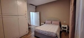 A bedroom with a bed, bedside tables, a wardrobe, and a door leading to another room.