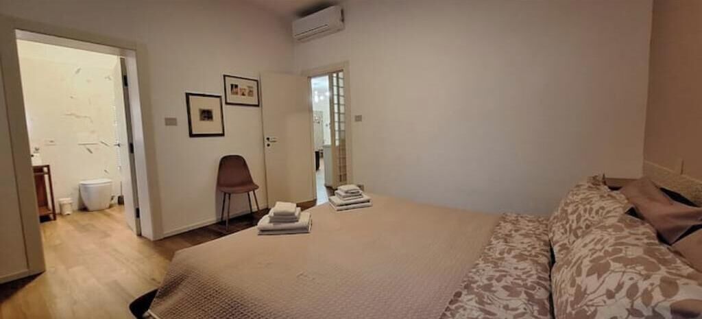 Una camera da letto con un letto, una sedia e un'anta che dà su un bagno.