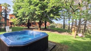Un jacuzzi en un patio trasero con césped, árboles y un edificio al fondo.