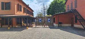 A courtyard with a covered seating area, a building with a red facade, and a parking gate.