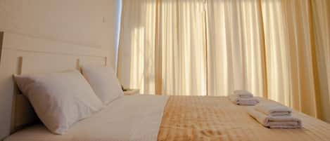 Habitación de hotel con cama, almohadas, mesita de noche, lámpara y ventana con cortinas.