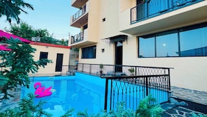 A multi-story building with balconies, a swimming pool with a pink flamingo decoration, and surrounding greenery. - Horizont Boutique Hotel (Telavi)