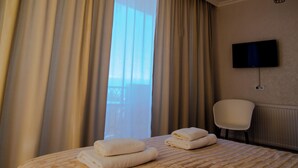 A hotel room with a bed, a chair, a television, and a window with curtains. - Horizont Boutique Hotel (Telavi)