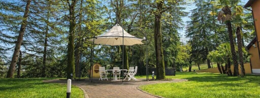 An outdoor seating area with a table and chairs under a canopy, surrounded by trees.