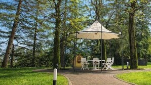 Ein Sitzbereich im Freien mit Tisch und Stühlen unter einer Markise, umgeben von Bäumen.